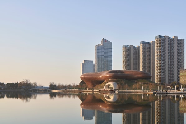A modern building with a unique curved roof, surrounded by high-rise buildings and a calm body of water reflecting its structure. - Liyang Marriott Hotel (Changzhou)