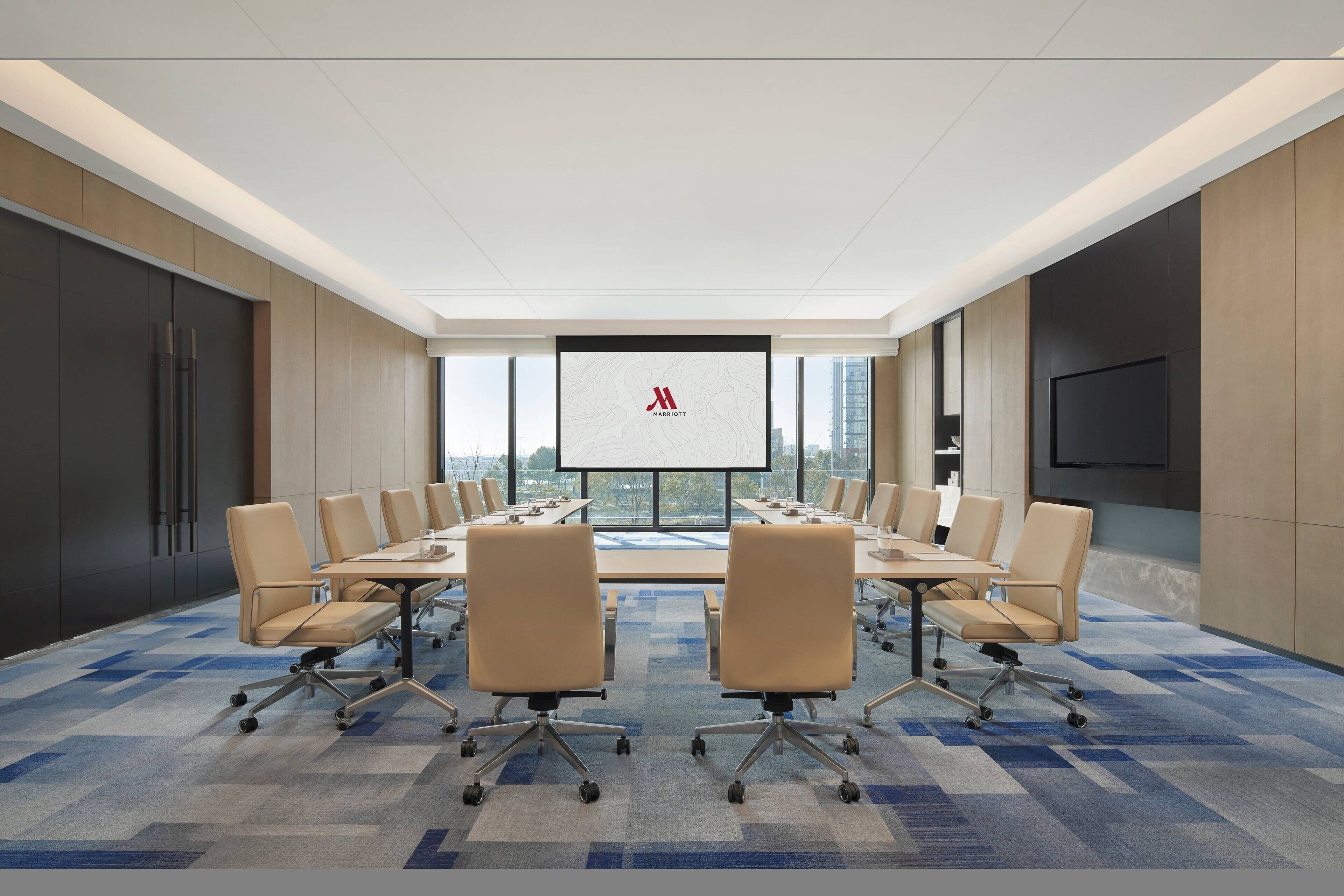 A modern conference room with a large table, comfortable chairs, a large screen, and a city view.