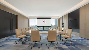 A modern conference room with a large table, comfortable chairs, a large screen, and a city view.