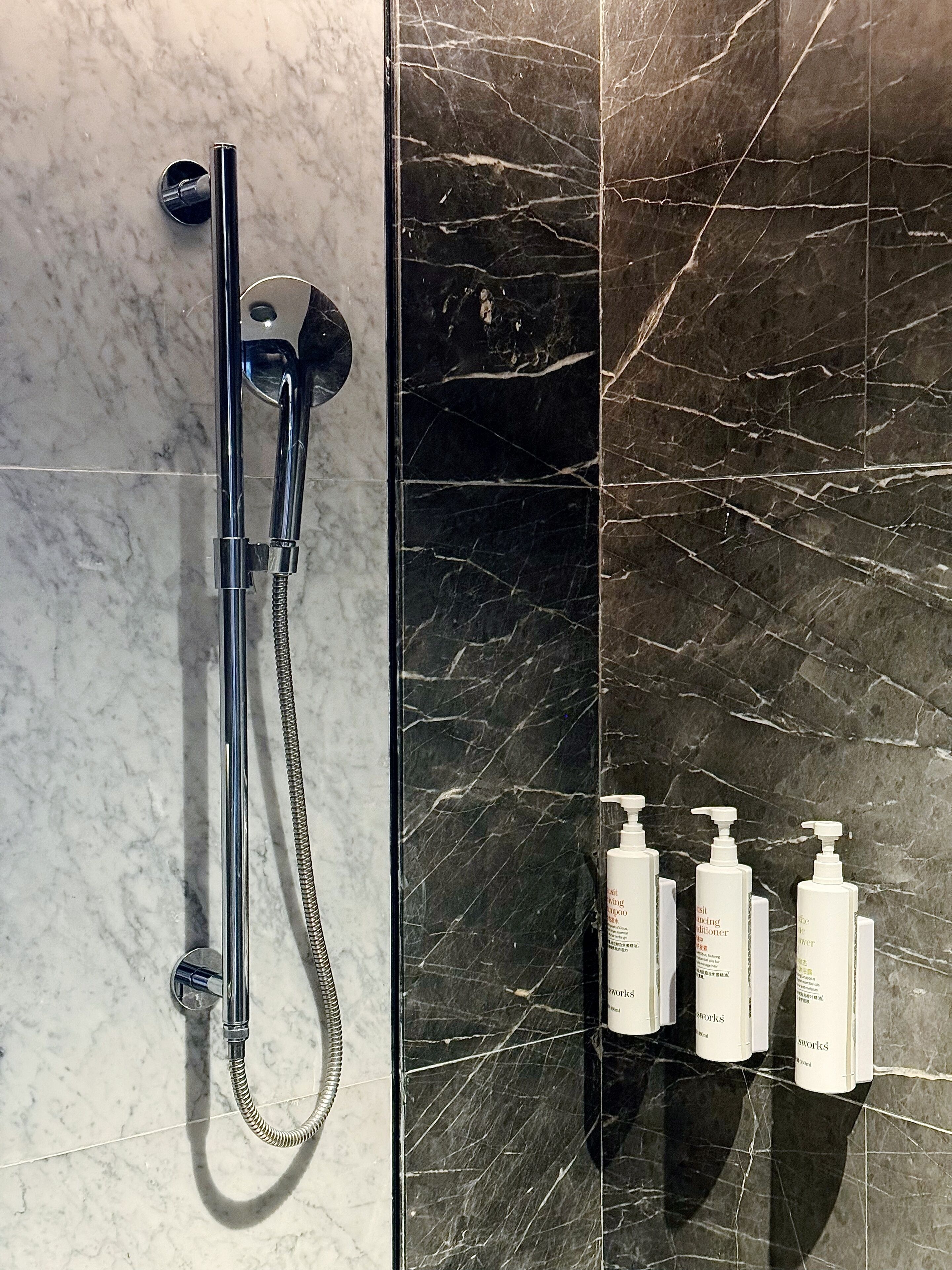 Un baño con ducha, pared de mármol y artículos de aseo.