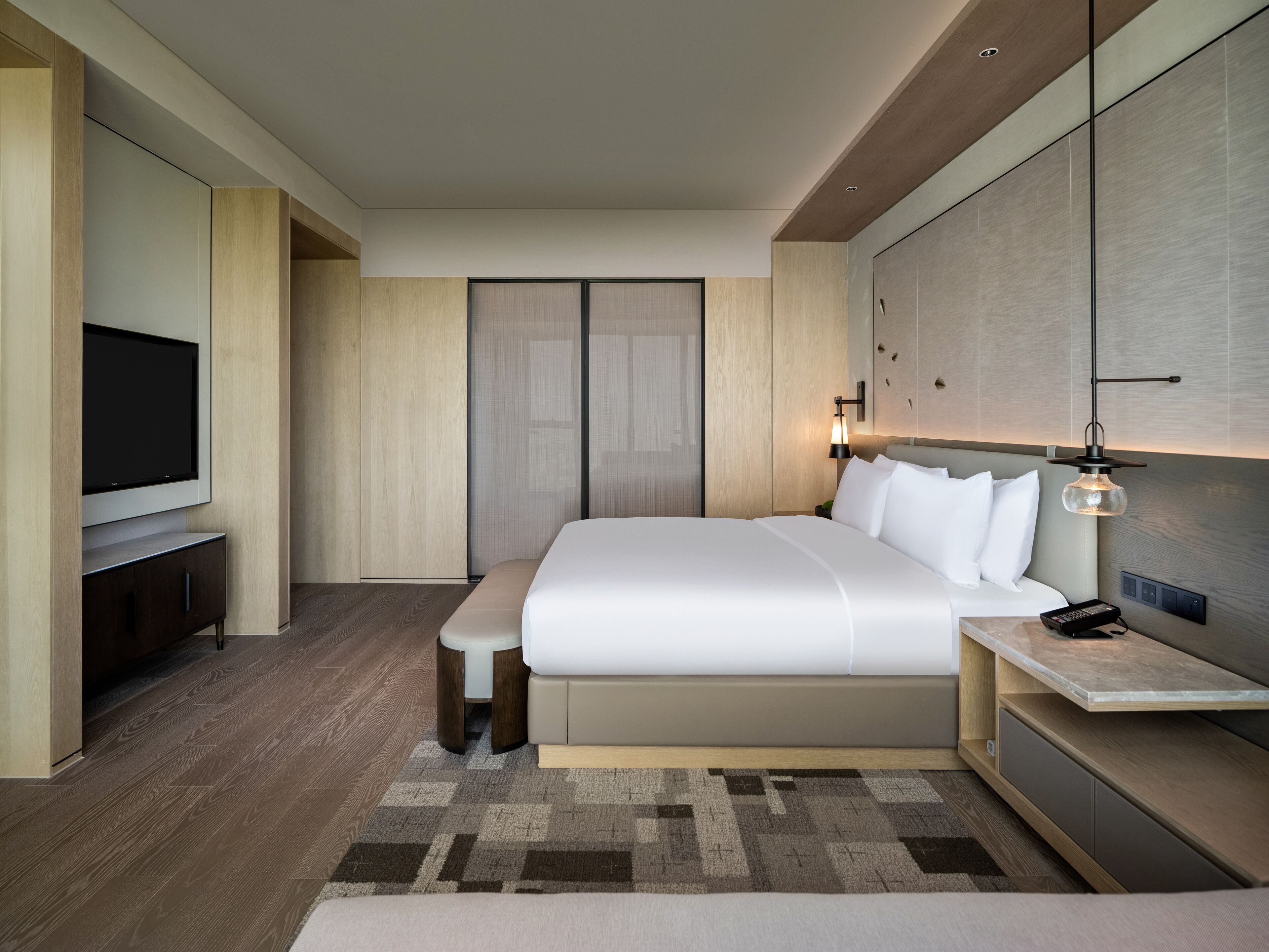 Ein modernes Hotelzimmer mit einem großen Bett, einem Flachbildfernseher, einem Nachttisch und einer Wandlampe.