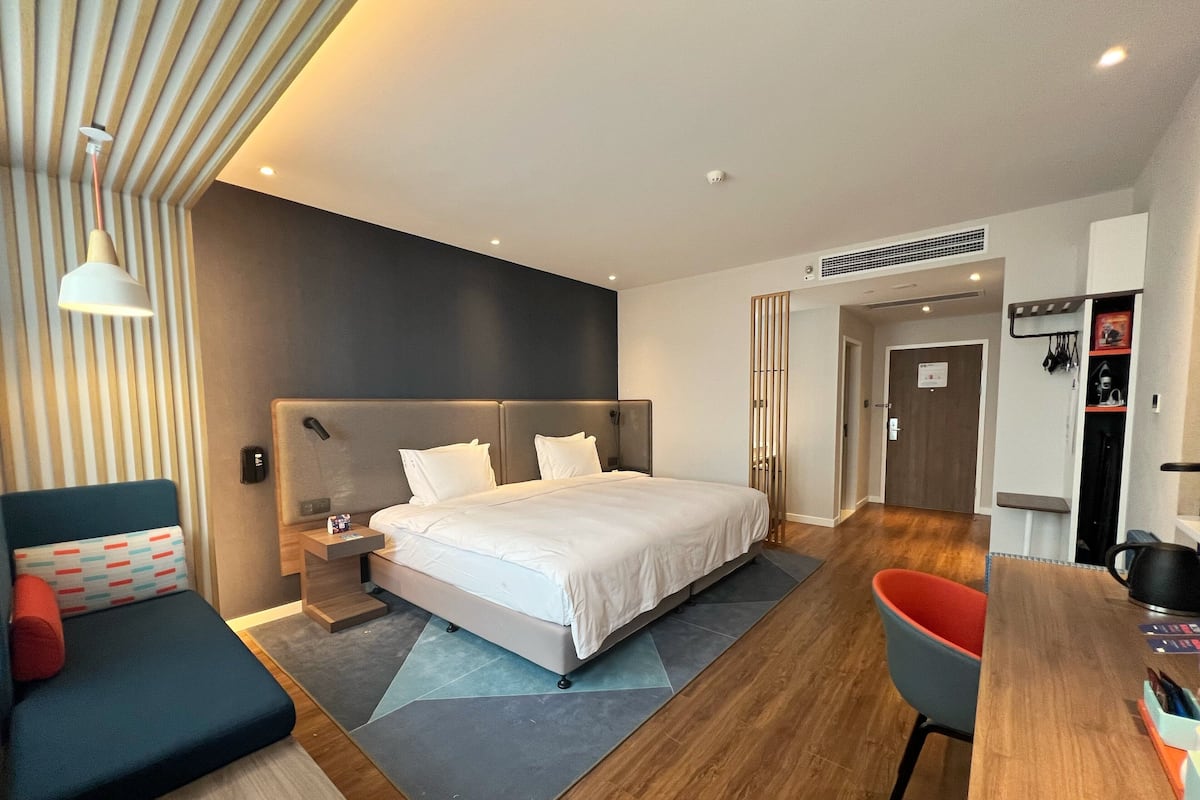 A modern hotel room with a large bed, a desk, a chair, and a sofa.