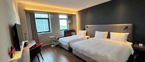 A hotel room with two beds, a desk, a chair, and a TV.