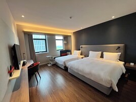 Quarto de hotel com duas camas, uma mesa, uma cadeira e uma televisão.