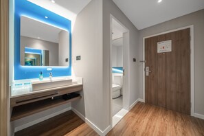 A modern bathroom with a large mirror, a vanity with a sink, and a wooden door.