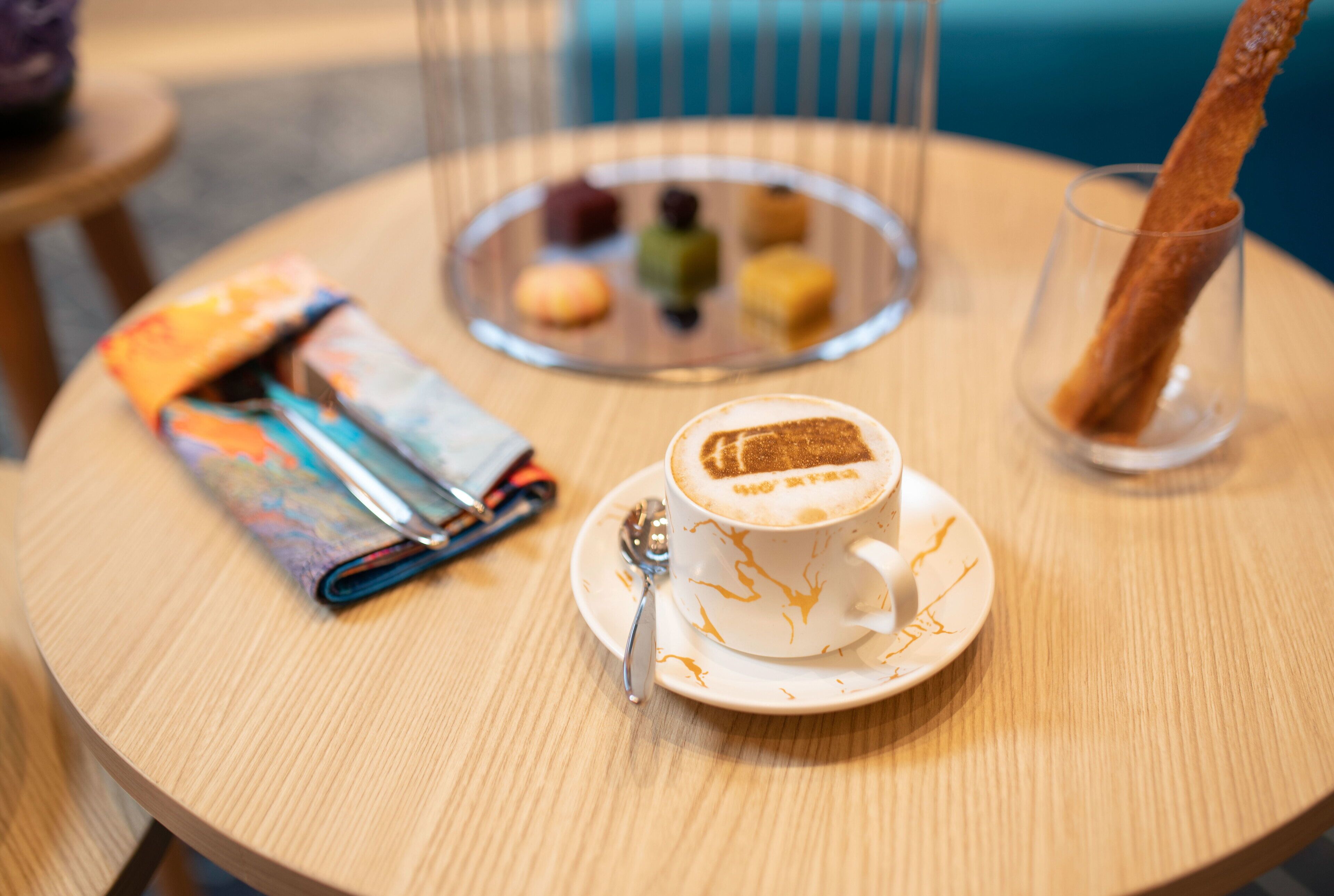 A round wooden table with a white cup of coffee, a pastry, and a glass of water.