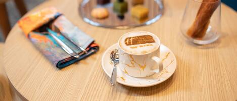 A round wooden table with a white cup of coffee, a pastry, and a glass of water.
