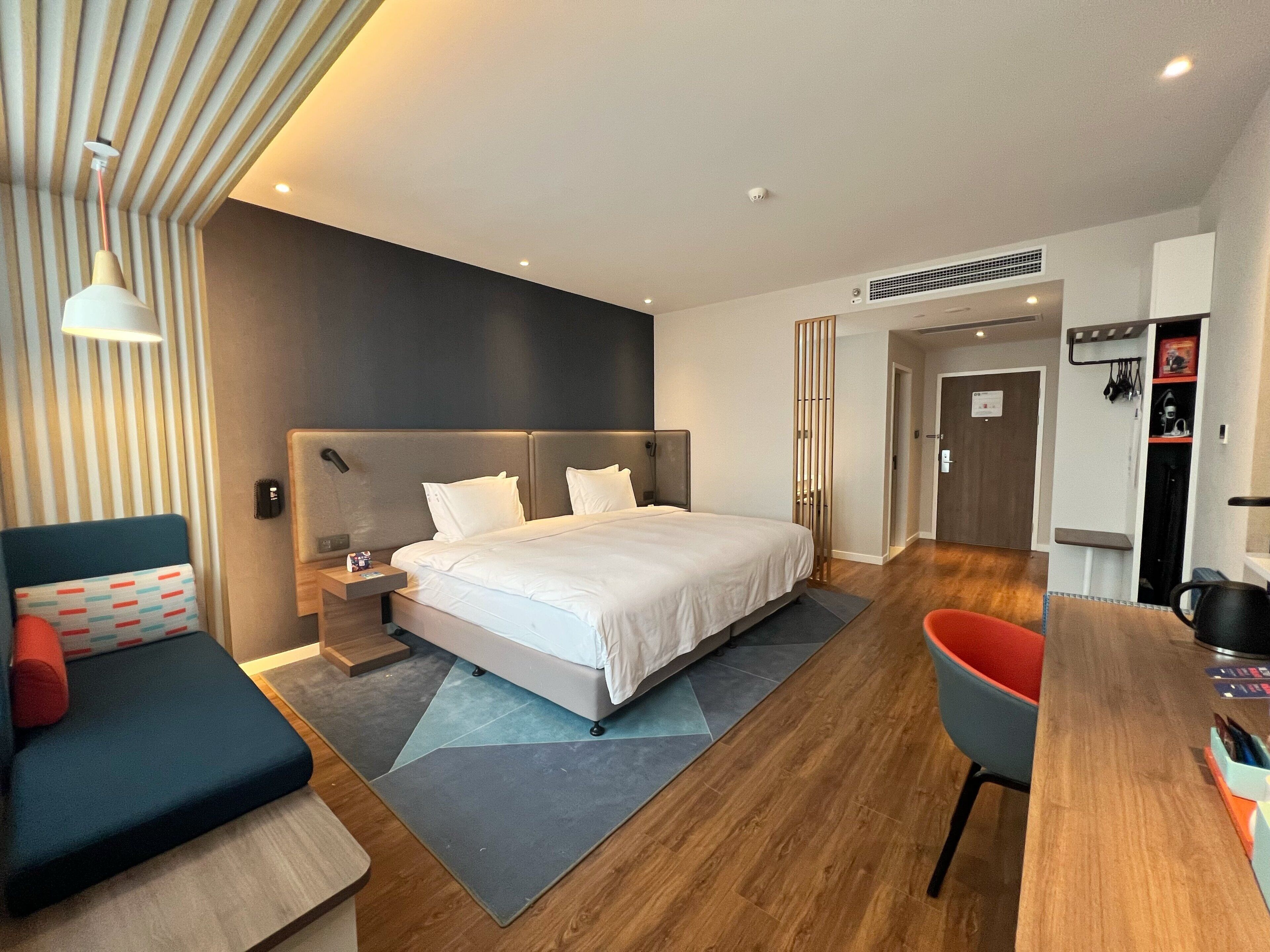 A modern hotel room with a large bed, a desk, a chair, and a sofa.
