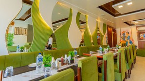 A restaurant with green booths, tables set with water bottles, glasses, and condiments. - Hotel Krishna by KeyMagics (Jaipur)