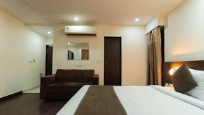 A hotel room with a bed, a brown sofa, a mirror, an air conditioning unit, and a door. - Hotel Krishna by KeyMagics (Jaipur)