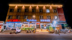 A hotel with a sign reading "Krishna Hotel" and a "Banquet Restaurant" sign below. There are motorcycles parked in front and a white car in front of the building. - Hotel Krishna by KeyMagics (Jaipur)