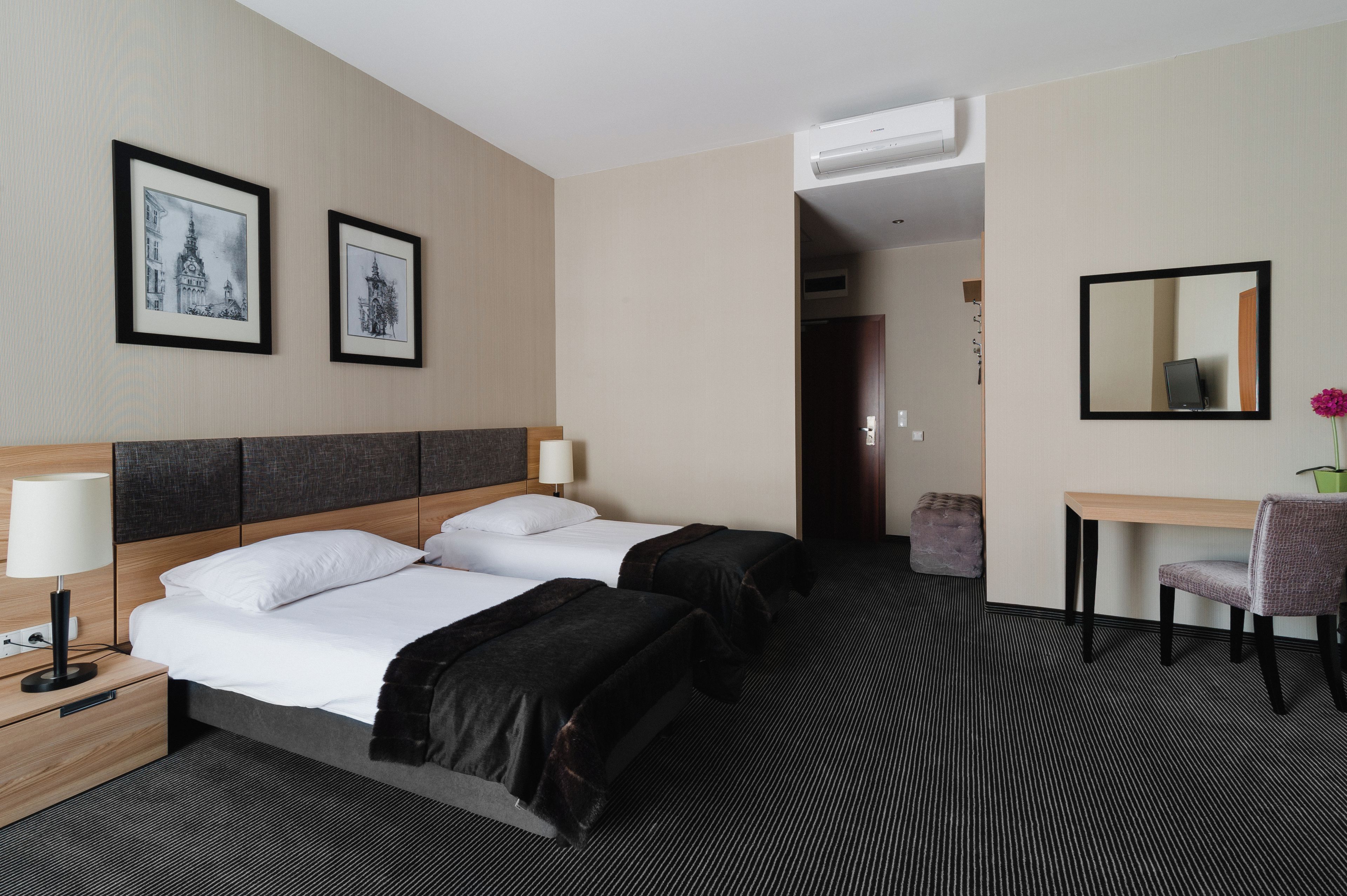 Habitación de hotel con dos camas, un escritorio, una silla, un espejo y dos cuadros en la pared.