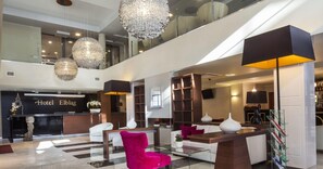A hotel lobby with a reception desk, seating area, and a staircase.