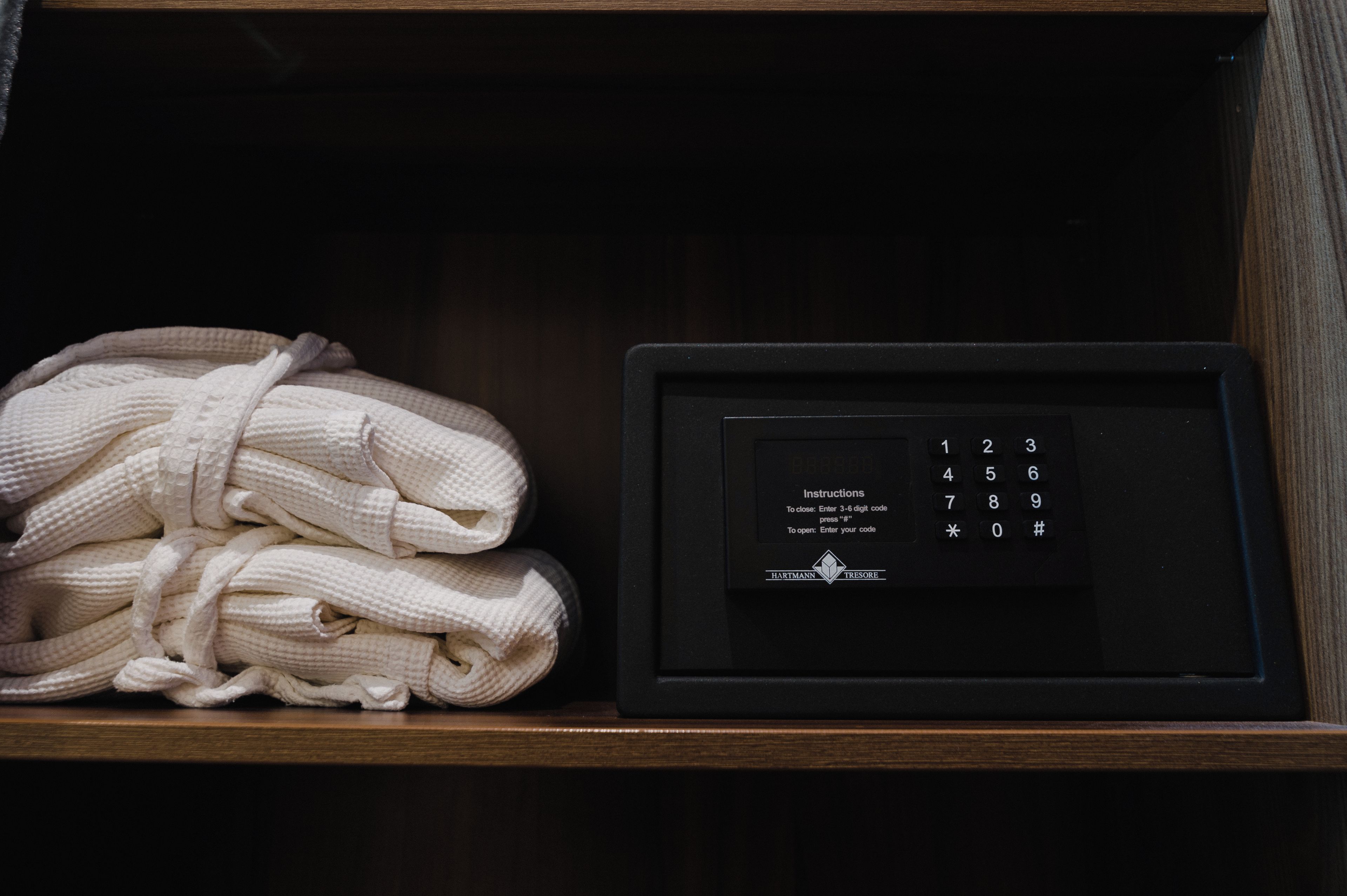 Estante de madeira com pilhas de robes brancos e um dispositivo eletrônico preto com teclado.