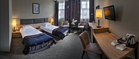 Hotellihuone, jossa on kaksi sänkyä, työpöytä, tuoli, televisio ja ikkuna, jossa on verhot.