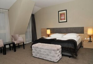 A hotel room with a bed, bedside tables, a chair, a small table, and a window with curtains. - Focus Hotel Premium Elbląg (Elblag)