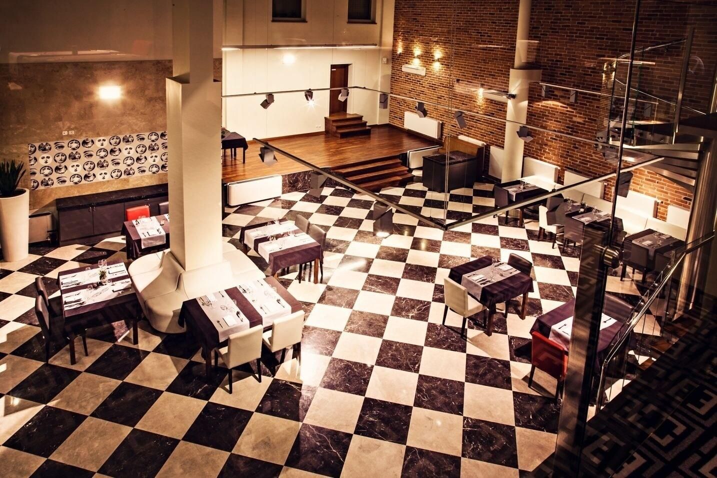 A hotel lobby with a checkered floor, seating areas, a staircase, and a wall with patterned artwork.