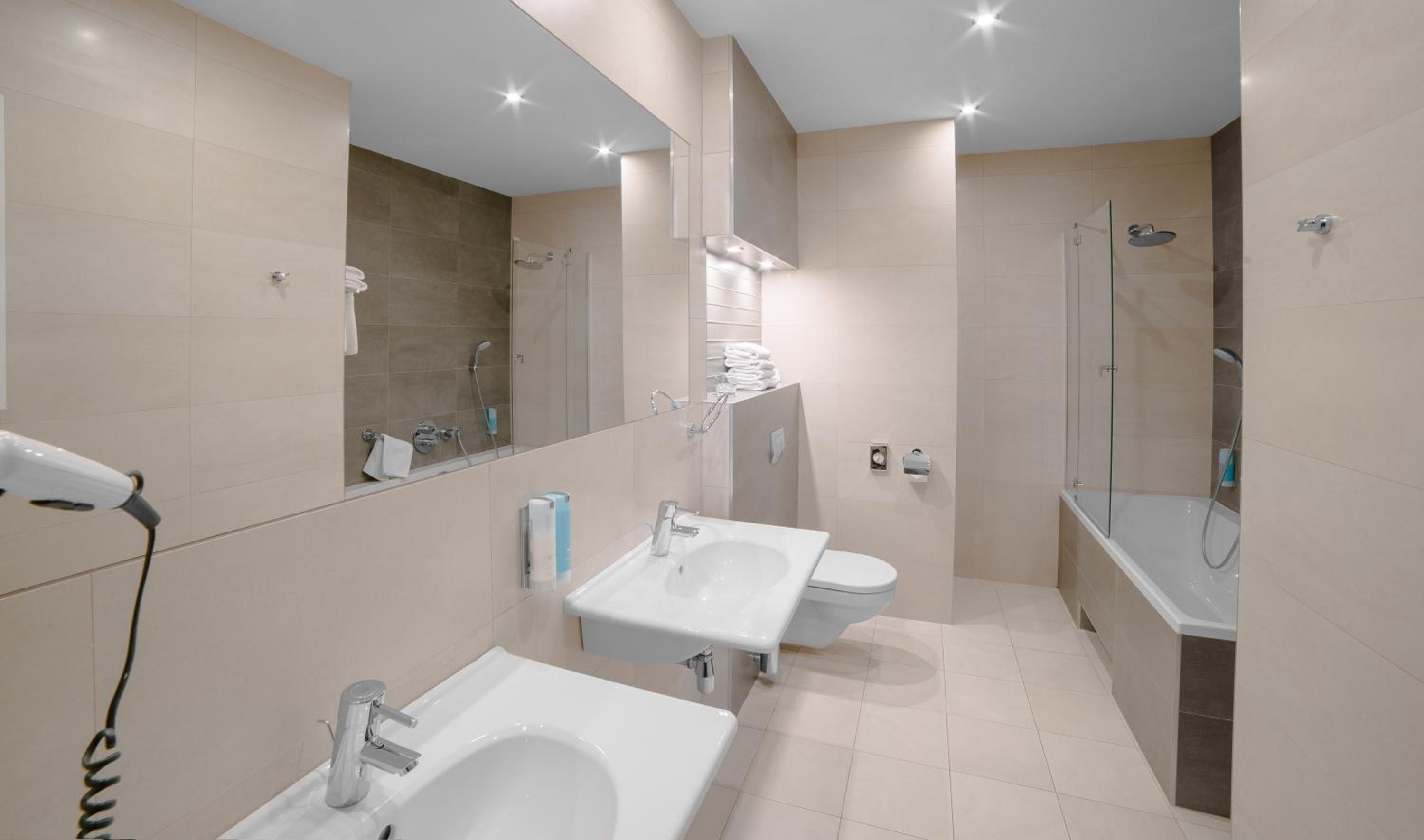 Un baño moderno con dos lavamanos, un inodoro, ducha y un espejo grande.