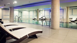 A modern indoor swimming pool with lounge chairs and a tiled floor. - Focus Hotel Premium Elbląg (Elblag)