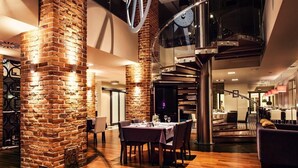 A modern interior with exposed brick walls, a spiral staircase, and a dining area with tables and chairs. - Focus Hotel Premium Elbląg (Elblag)