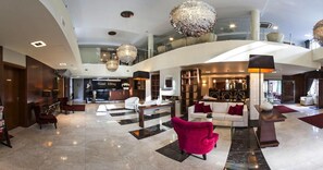 A spacious hotel lobby with a check-in counter, seating area, and a bar/lounge.