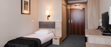 Et hotelværelse med en seng, et natbord, en lampe og et skrivebord med en computer.