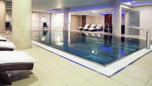 Una piscina interior con sillones de descanso y suelo de baldosas.