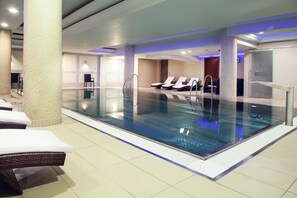 An indoor swimming pool with lounge chairs and a tiled floor.