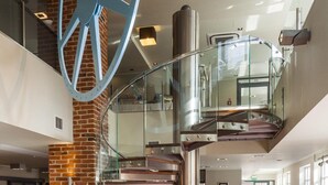 A modern interior with a glass staircase, metal railings, and a brick wall. - Focus Hotel Premium Elbląg (Elblag)