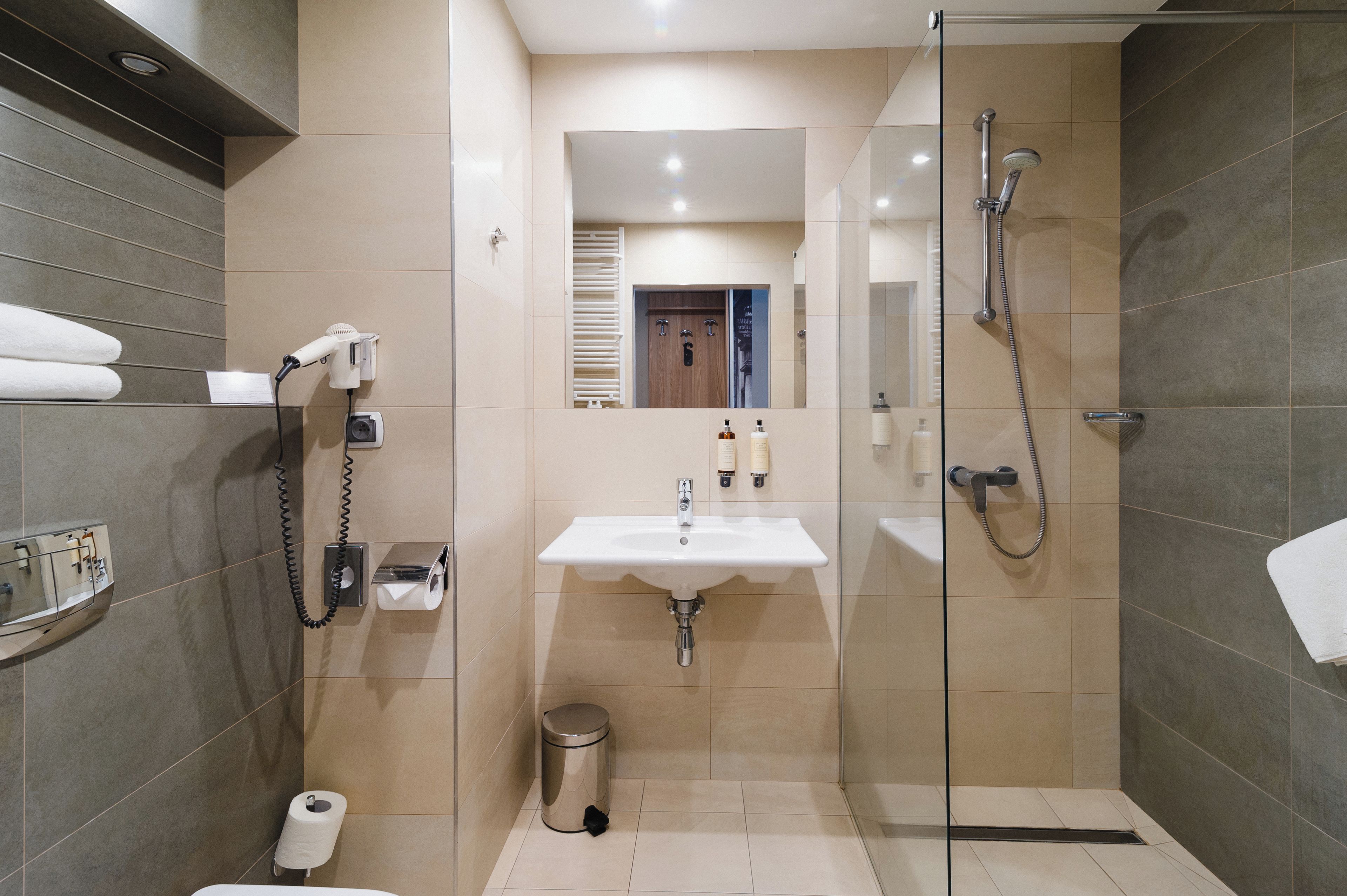 A modern bathroom with a glass shower enclosure, a sink with a mirror above, and a hairdryer on a wall-mounted station.