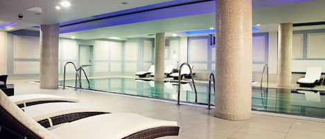 A modern indoor swimming pool with lounge chairs and a tiled floor.