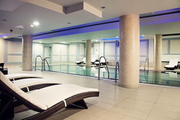 A modern indoor swimming pool with lounge chairs and a tiled floor. - Focus Hotel Premium Elbląg (Elblag)