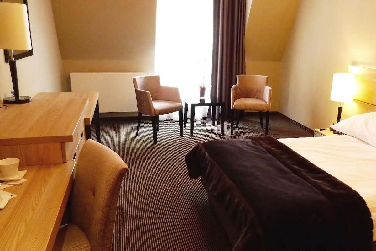 A hotel room with a bed, two chairs, a desk, and a lamp.