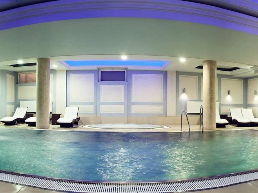 Una amplia piscina interior con numerosas tumbonas y un área de jacuzzi central.