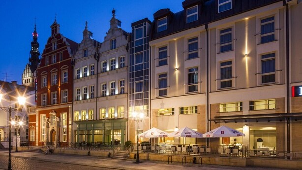 A historic building with a modern restaurant on the ground floor, featuring outdoor seating and a well-lit facade. - Focus Hotel Premium Elbląg (Elblag)