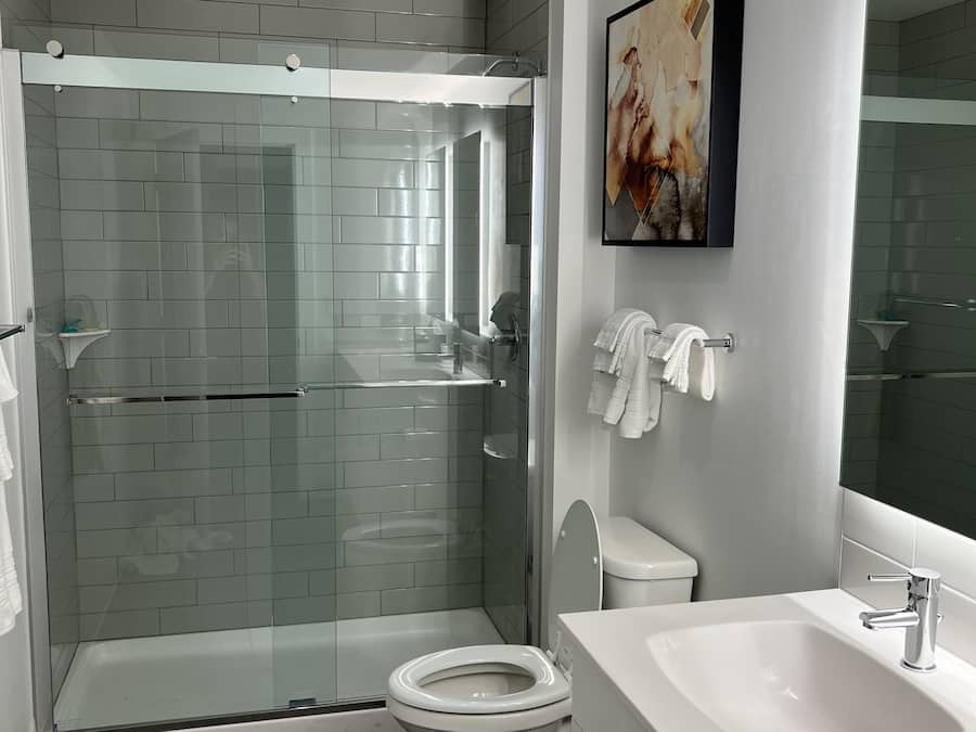 Ein modernes Badezimmer mit einer Duschkabine, einer weißen Toilette und einem großen Spiegel.