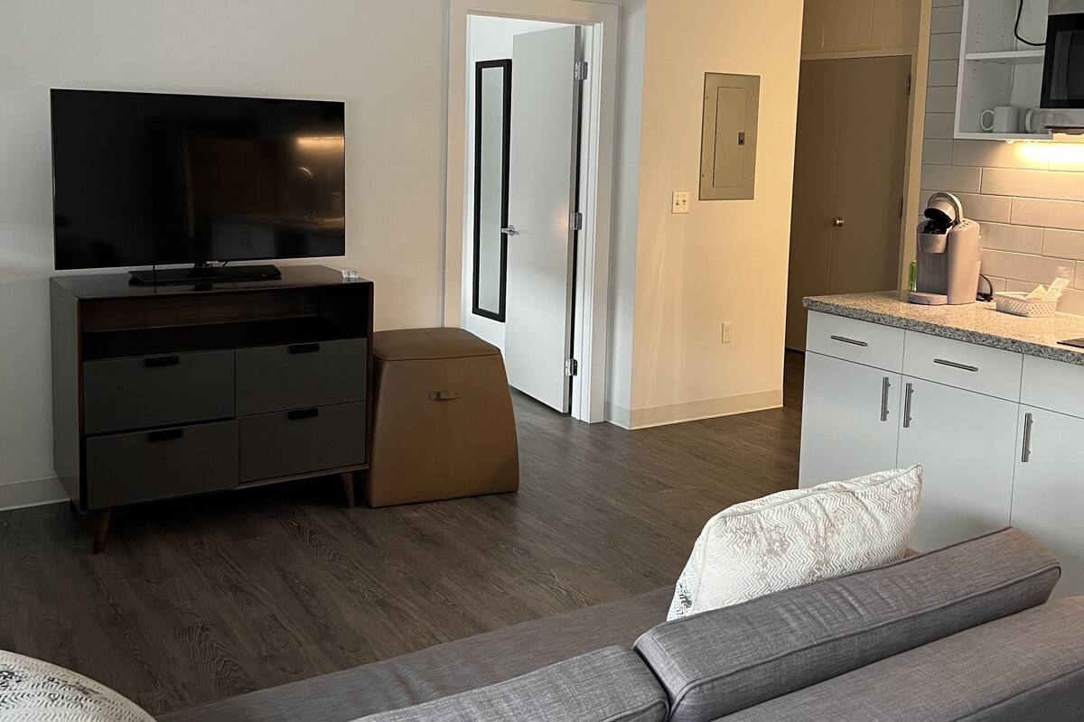 A modern living room with a flat-screen TV, a sofa, and a kitchen area with a microwave and cabinets.