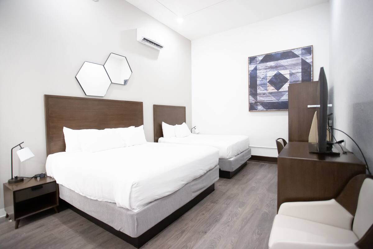 A hotel room with two beds, a desk, a chair, and a TV.