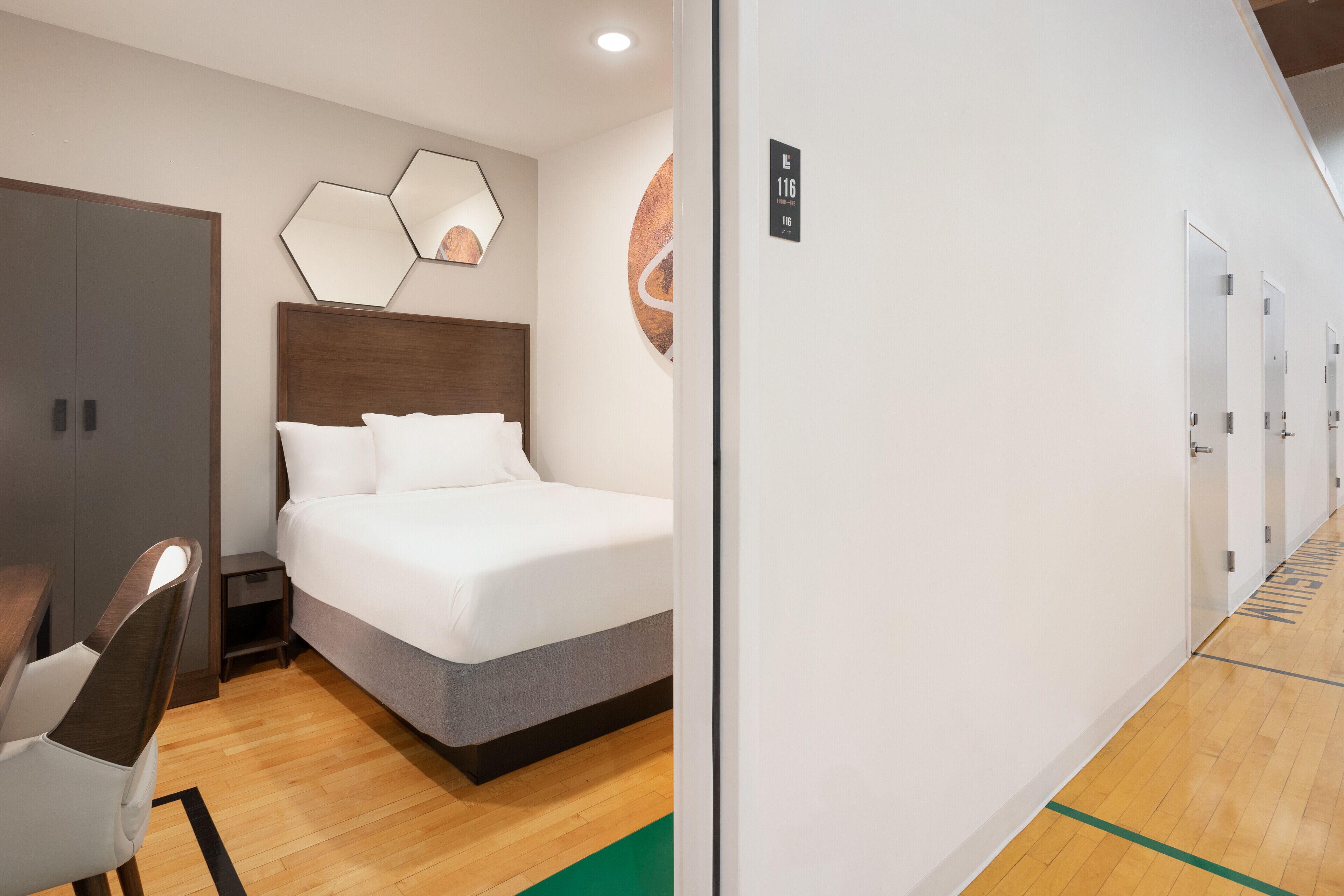 Habitación de hotel con cama, escritorio y armario. Se observa una puerta con un letrero encima.