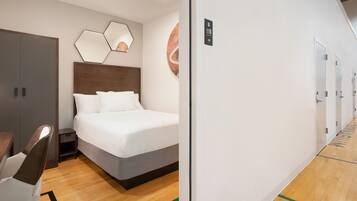 Habitación de hotel con cama, escritorio y armario. Se observa una puerta con un letrero encima.
