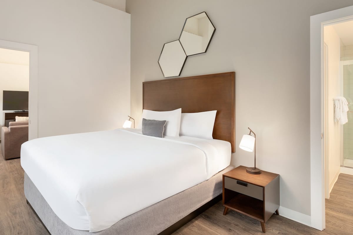 A hotel room with a large bed, a wooden headboard, a bedside table with a lamp, and a wall-mounted mirror.