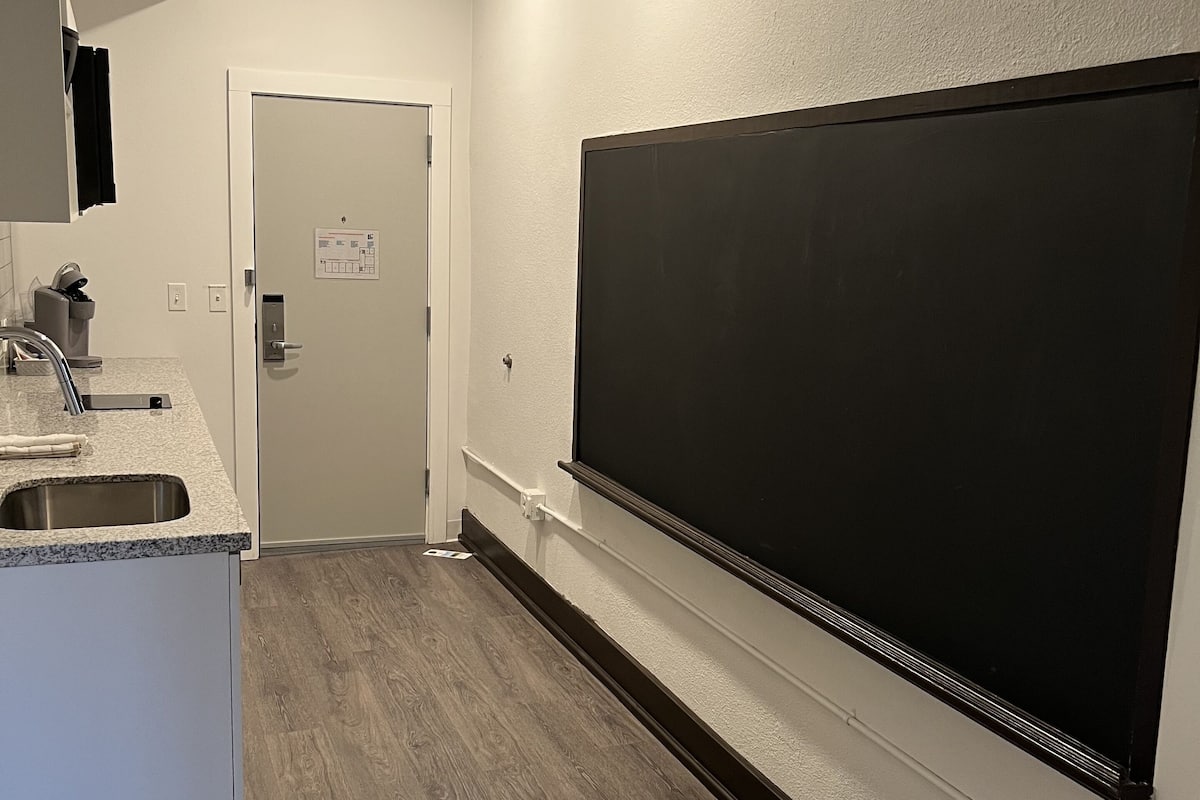 A modern kitchen with a large black screen mounted on the wall, a built-in sink, and a door leading to another room.