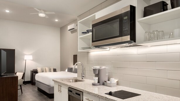 A modern hotel room with a kitchenette, a bed, a desk, and a bathroom.