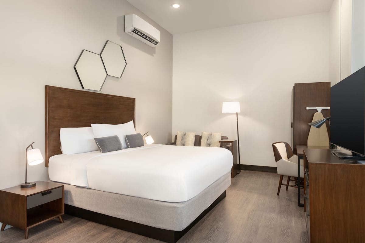 A hotel room with a large bed, bedside tables, a desk, a chair, and a TV.