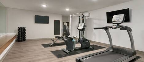 Un gimnasio moderno con cinta de correr, elíptica y máquina de pesas.