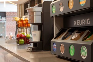 A coffee machine with various coffee pod options and a basket of fruits on the counter.