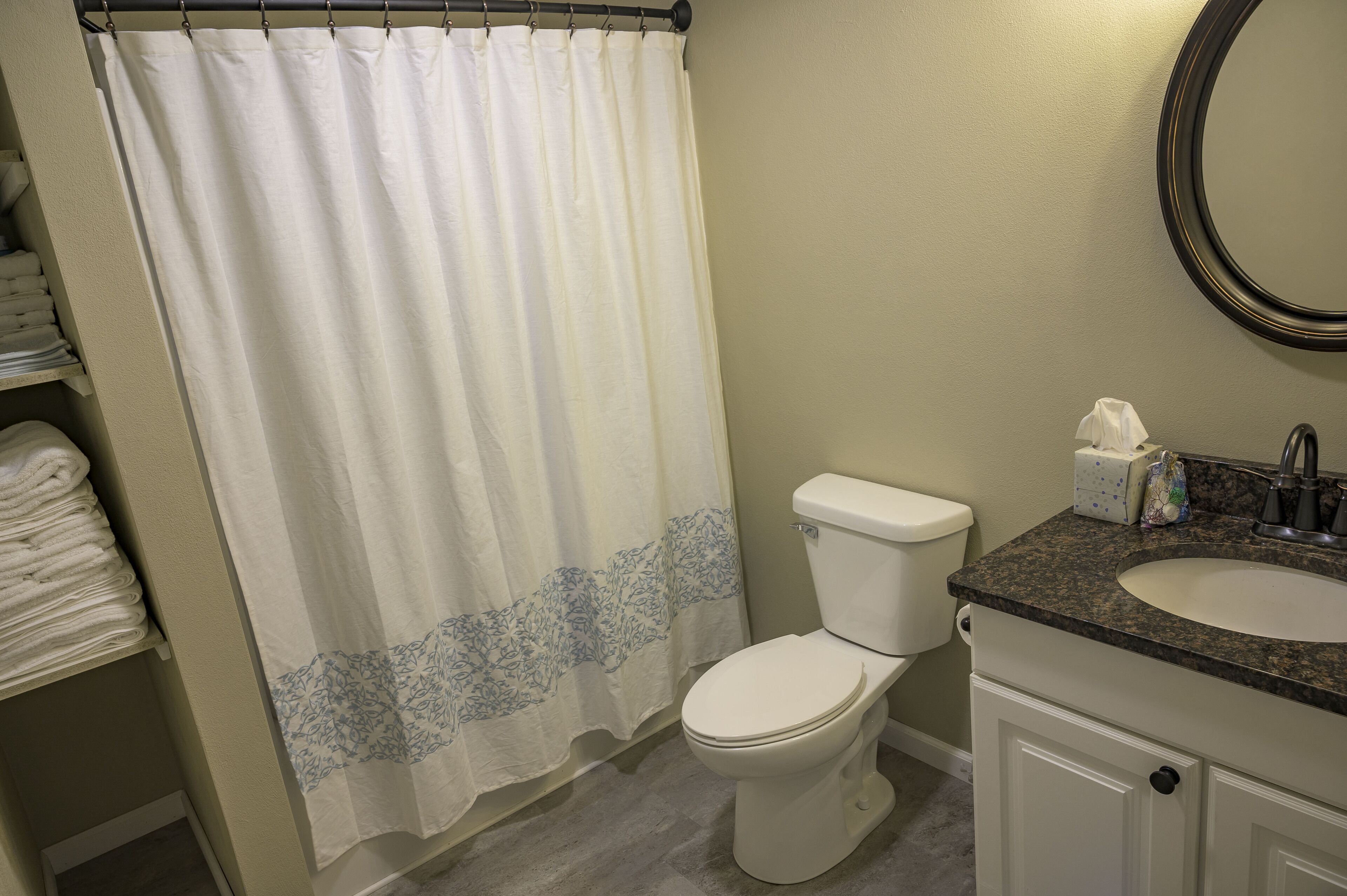 Een badkamer met een wit toilet, een wastafel met een granieten blad en een douchegordijn met een blauw bloemenmotief.