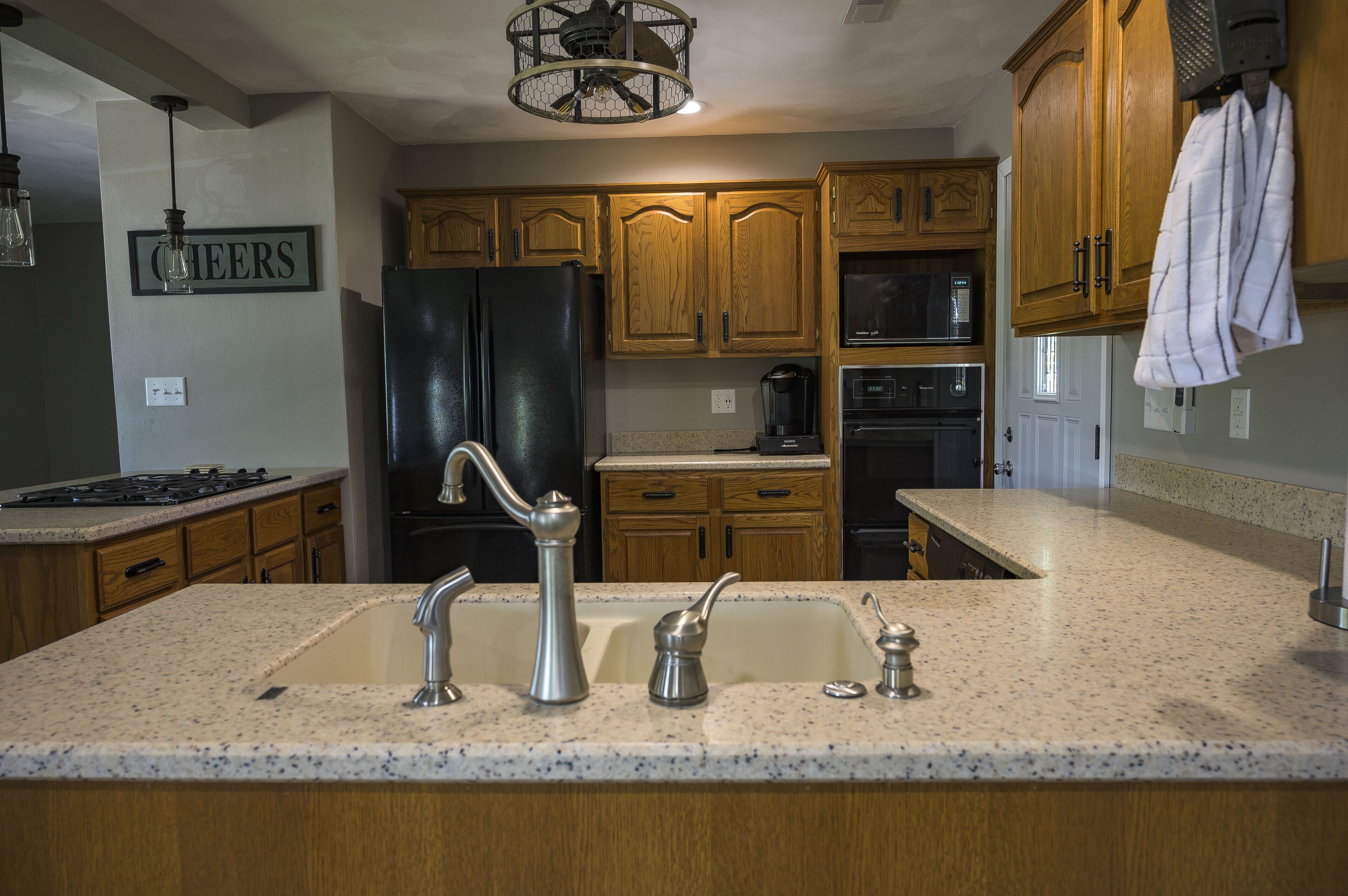 A kitchen with wooden cabinets, a black refrigerator, a granite countertop, and a 'CHEERS' sign on the wall.