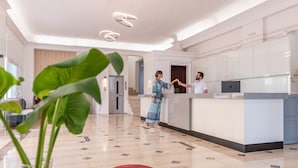 Un hall d’hôtel à l’esthétique moderne, comprenant un comptoir d’accueil, un escalier et un pot de fleurs en premier plan.