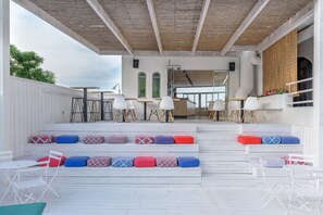 An outdoor seating area with white tables and chairs, colorful cushions, and a wooden ceiling. - Azure Mare Hotel (Hersonissos)